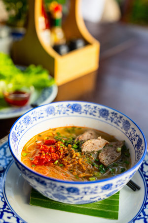 A bowl of Khao Piak Sen, a traditional Laotian noodle soup, served with rice noodles, meat, chili,...