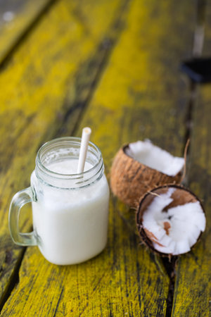 A creamy coconut milkshake served in a mason jar with a straw, accompanied by fresh coconut halves...