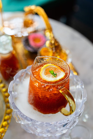 A refreshing glass of iced tea served in a crystal pitcher, garnished with a slice of lemon and a...