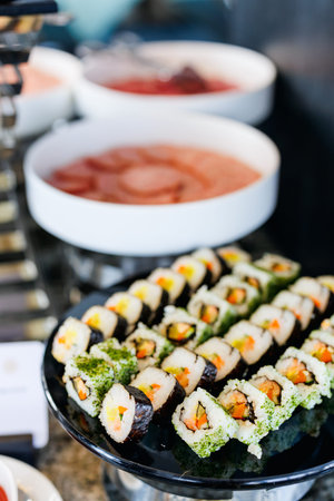 A display of various sushi rolls on a black platter, featuring seaweed wraps, rice, and colorful...