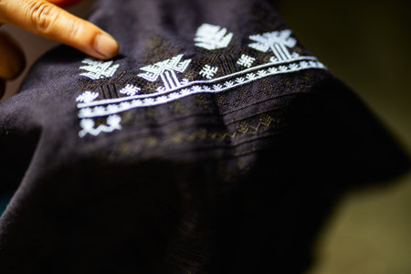 Detailed view of black H'mong traditional clothing from Sapa, Vietnam. The intricate white embroidery patterns are highlighted as a finger gently points to the designの写真素材
