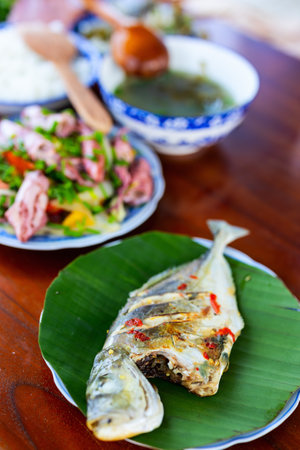 A whole grilled fish served on a banana leaf, accompanied by a colorful spread of traditional Vietnamese dishes, including fresh salad and soupの写真素材