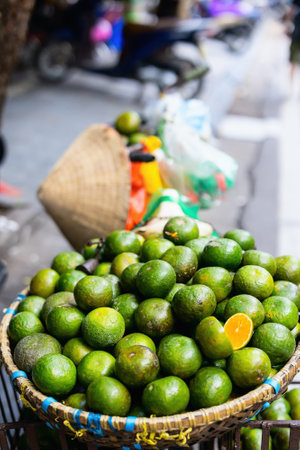 A large woven basket filled with vibrant green limes, displayed at a street market. One lime is cut open to reveal the bright orange flesh inside.の写真素材
