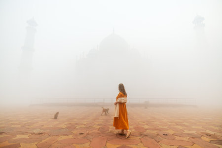 A woman in an orange dress stands on the Taj Mahal's terrace, surrounded by dense fogの写真素材