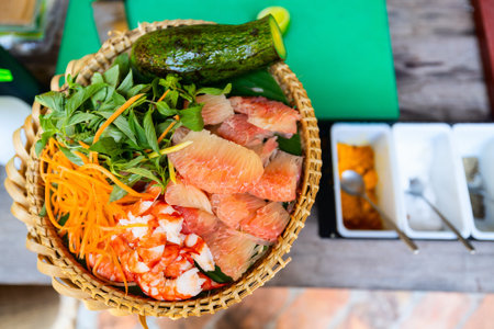 A basket containing fresh ingredients for a pomelo prawn salad, including peeled pomelo segments, cooked prawns, shredded carrot, fresh herbs, and an avocadoの写真素材