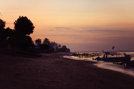 A golden sunset against the backdrop of boats, trees and wavesの写真素材