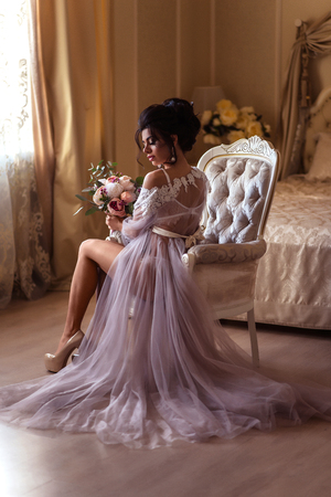 Boudoir morning of the bride. The bride sits on a chair with flowersの写真素材