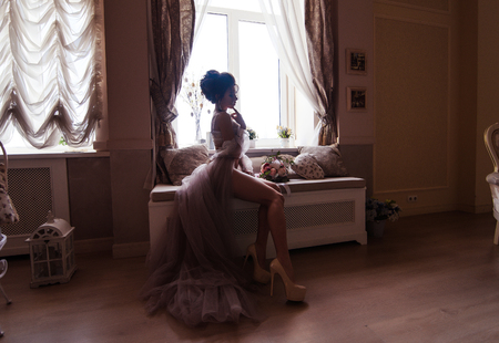 Boudoir morning of the bride. Bride stay near the window with flowersの写真素材