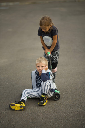 Two children, boy and girl, playing with scooters on the street.