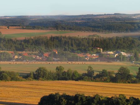 Hilly landscape in early evening at the end of summer, light haze of fog around village in valley, plowed fieldsの写真素材