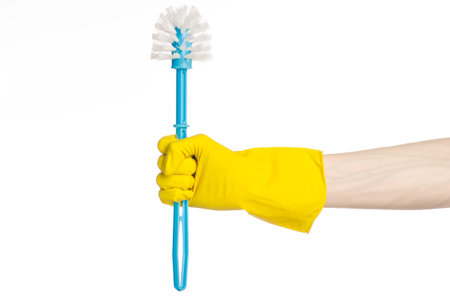 Cleaning the house and cleaning the toilet: human hand holding a blue toilet brush in yellow...