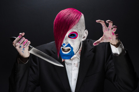 Clown and Halloween theme: Scary clown with pink hair in a black suit with a knife in his hand on a dark backgroundの写真素材