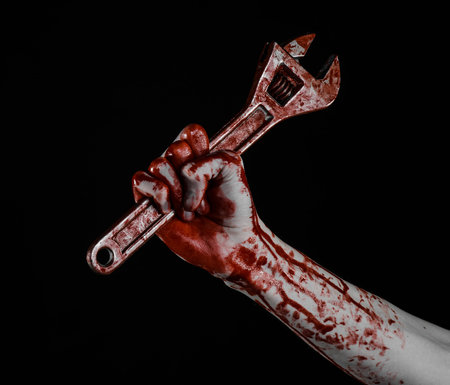 Halloween theme: bloody hand holding a big wrench on a black background studioの写真素材