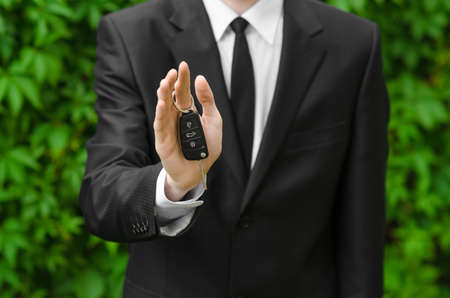 New car and business theme: a man in a black suit holds the keys of a new car on a background of green grass studioの写真素材