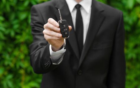 New car and business theme: a man in a black suit holds the keys of a new car on a background of green grass studioの写真素材