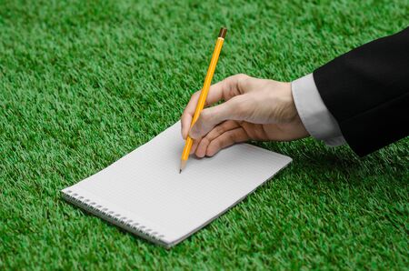 Day of knowledge and business topic: the hand of man in a black suit holding a notebook and pencil top view on a background of green grass studioの写真素材