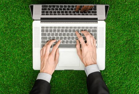 Work outdoors and businessman topic: human hands show the gestures in a black suit and an open notebook on a background of green grass top view studioの写真素材
