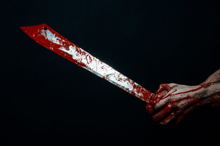 Bloody halloween theme: bloody hands holding a bloody machete isolated on black background in studio