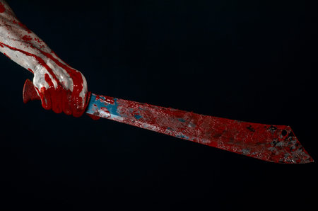 Bloody halloween theme: bloody hands holding a bloody machete isolated on black background in studio