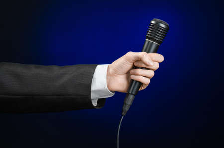 Business speech and topic: a man in a black suit holding a black microphone on a dark blue background in studioの写真素材