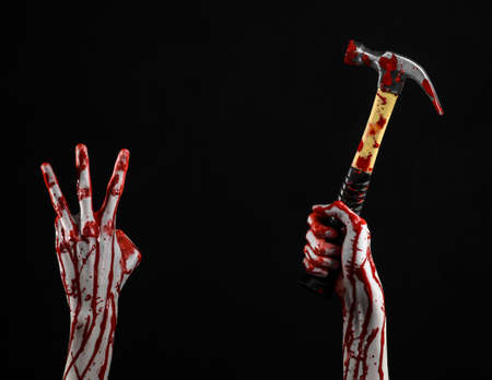 Bloody halloween theme: bloody hand holding a bloody hammer isolated on a black backgroundの写真素材