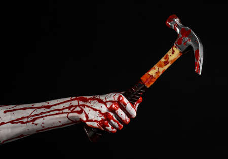 Bloody halloween theme: bloody hand holding a bloody hammer isolated on a black backgroundの写真素材