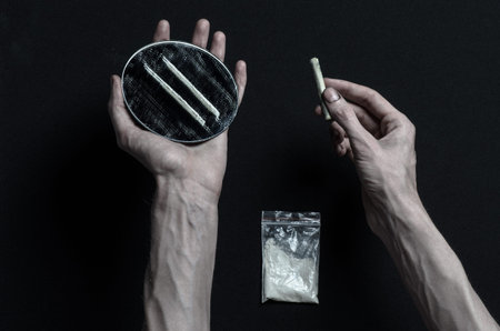 The fight against drugs and drug addiction topic: hand addict lies on a dark table and around it are...