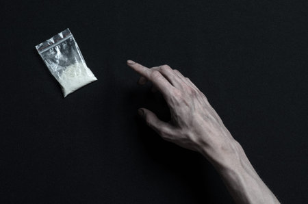 The fight against drugs and drug addiction topic: hand addict lies on a dark table and around it are drugsの写真素材