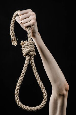 Lynching and suicide theme: man's hand holding a loop of rope for hanging on black isolated background studioの写真素材