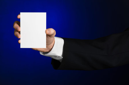 Business and advertising topic: Man in black suit holding a white blank card in his hand on a dark...