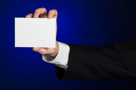 Business and advertising topic: Man in black suit holding a white blank card in his hand on a dark blue background in studio isolatedの写真素材