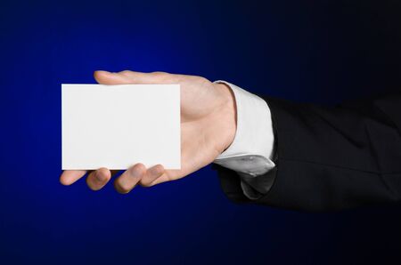 Business and advertising topic: Man in black suit holding a white blank card in his hand on a dark blue background in studio isolatedの写真素材