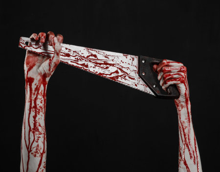 Halloween theme: bloody hand holding a bloody saw on a black background