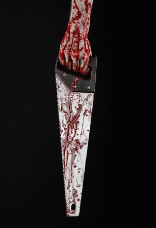 Halloween theme: bloody hand holding a bloody saw on a black backgroundの写真素材