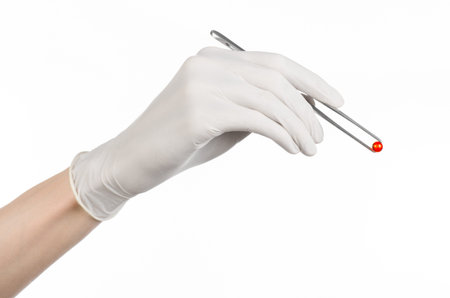 Pharmacology and Medical theme: doctor's hand in a white glove holding tweezers with red pill capsule isolated on white background in studioの写真素材