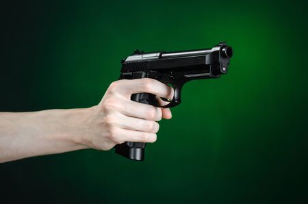 Firearms and murderer topic: human hand holding a gun on a dark green background isolatedの写真素材