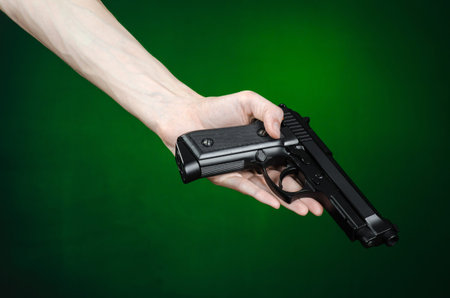 Firearms and murderer topic: human hand holding a gun on a dark green background isolated