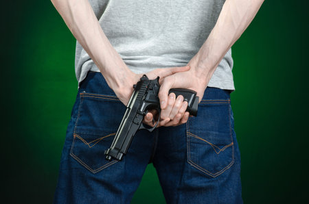 Firearms and murderer topic: man in a gray t-shirt holding a gun on a dark green background isolated