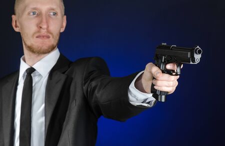 Firearms and security topic: a man in a black suit holding a gun on a dark blue background in studioの写真素材