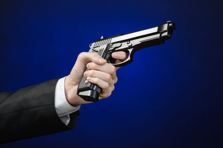 Firearms and security topic: a man in a black suit holding a gun on a dark blue background in studio