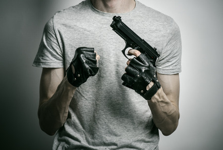 Horror and firearms topic: the killer with a gun in his hand in black gloves on a gray backgroundの写真素材