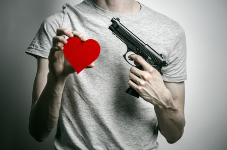 Horror and firearms topic: suicide with a gun in his hand and a red heart on a gray backgroundの写真素材