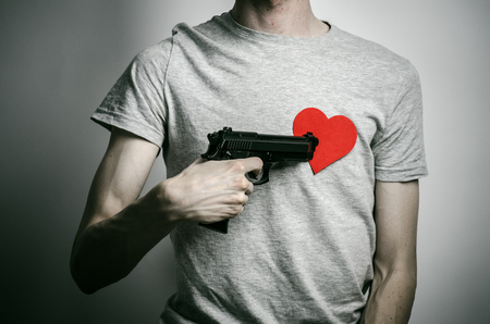 Horror and firearms topic: suicide with a gun in his hand and a red heart on a gray backgroundの写真素材