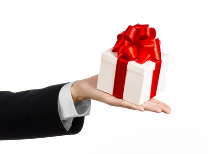 The theme of celebrations and gifts: a man in a black suit holding a exclusive gift wrapped in white box with red ribbon and bow, the most beautiful gift isolated on white backgroundの写真素材
