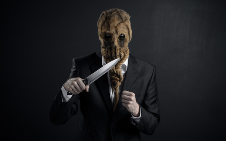 Fear and Halloween theme: a brutal killer in a mask holding a knife on a dark backgroundの写真素材