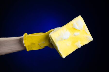 Cleaning the house and sanitation topic: Hand holding a yellow sponge wet with foam on a dark blue backgroundの写真素材