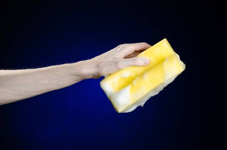 Cleaning the house and sanitation topic: Hand holding a yellow sponge wet with foam on a dark blue backgroundの写真素材