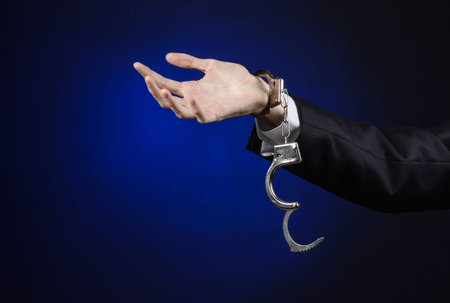 Corruption and bribery theme: businessman in a black suit with handcuffs on his hands on a dark blue...