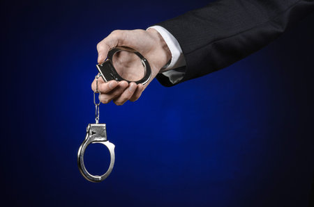 Corruption and bribery theme: businessman in a black suit with handcuffs on his hands on a dark blue...