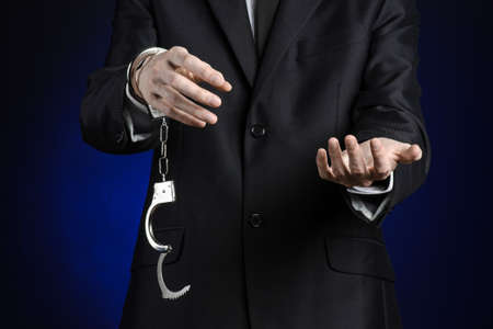 Corruption and bribery theme: businessman in a black suit with handcuffs on his hands on a dark blue background isolatedの写真素材